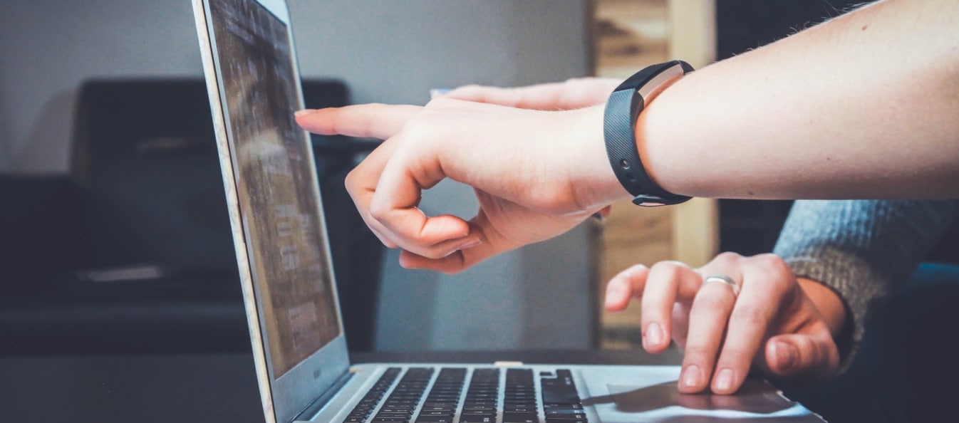 An image of a laptop from the side with two hands pointing at the screen and a third hand using the trackpad