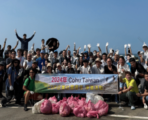 A group of over 50 people smiling and waving their hands with a beach in the background. They are holding a banner that reads 2024 Cohu Taiwan and over 10 pink plastic bags in the front