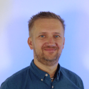 Headshot of a man wearing a dark blue collared shirt smiling with a neon blue background