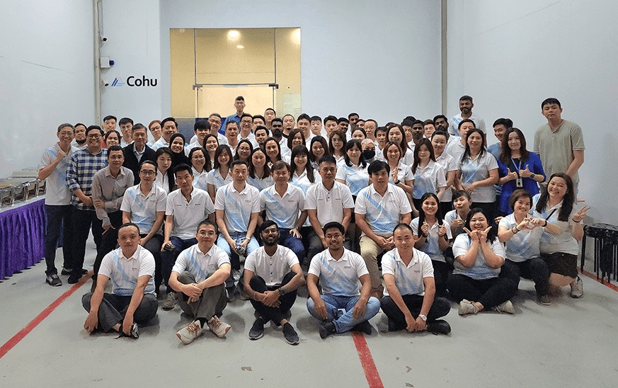 A group of about 80 men and women smiling for a picture in a tall room with white walls and EQT written on the back wall.